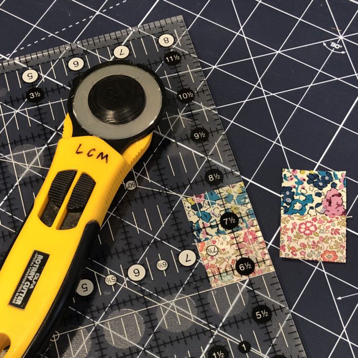Scrappy Liberty Patchwork Pincushion by Guest May Chappell by popular quilting blog, Diary of a Quilter: image of a rotary cutter, cutting board, and Liberty Lawns fabric.