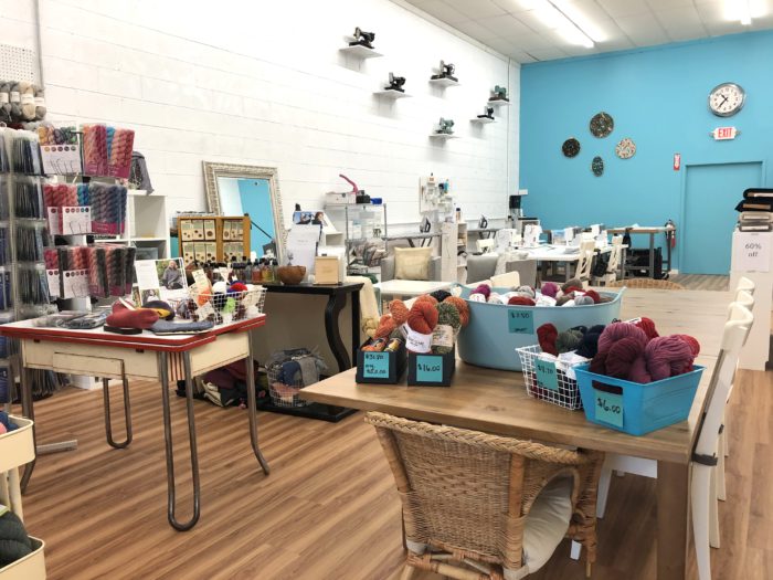 Pintuck & Purl - Modern Fabric and Knitting Shop by popular quilting blog, Diary of a Quilter: image of baskets with balls of yarn inside, and sewing tables with sewing machines inside Pintuck and Purl.