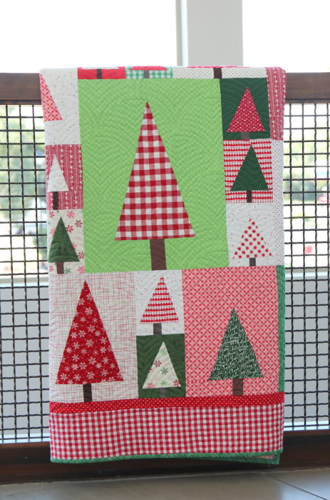 New Patchwork Forest Quilt Pattern: Pine Hollow Version by popular quilting blog, Diary of a Quilter: image of a red, white, and green patchwork forest tree quilt draped over a stair banister.