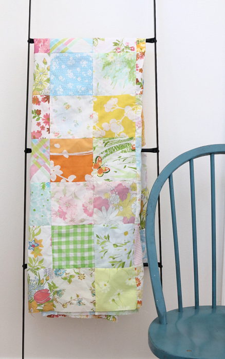 In Search of my Sewing Mojo and Other Tales of Summer by popular sewing blog, Diary of a Quilter: image of a pastel block quilt hanging on a decorative black ladder that's leaning against a wall.