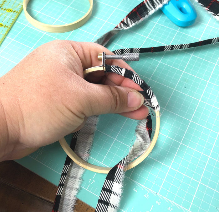 Christmas in July - Hand Stitched Christmas Ornament Tutorial by popular sewing blog, Diary of a Quilter: image of a hand wrapping a ¾" strip of black, white, and red fabric around a 3" embroidery hoop.