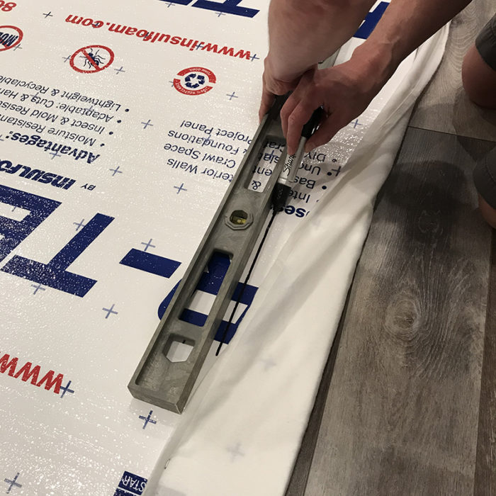 How to Build a Quilt Design Wall by Christa Watson by popular quilting blog, Diary of a Quilter: image of a man drawing a straight line with a permanent black marker 5 inches away from the edge of a foam core insulation board.