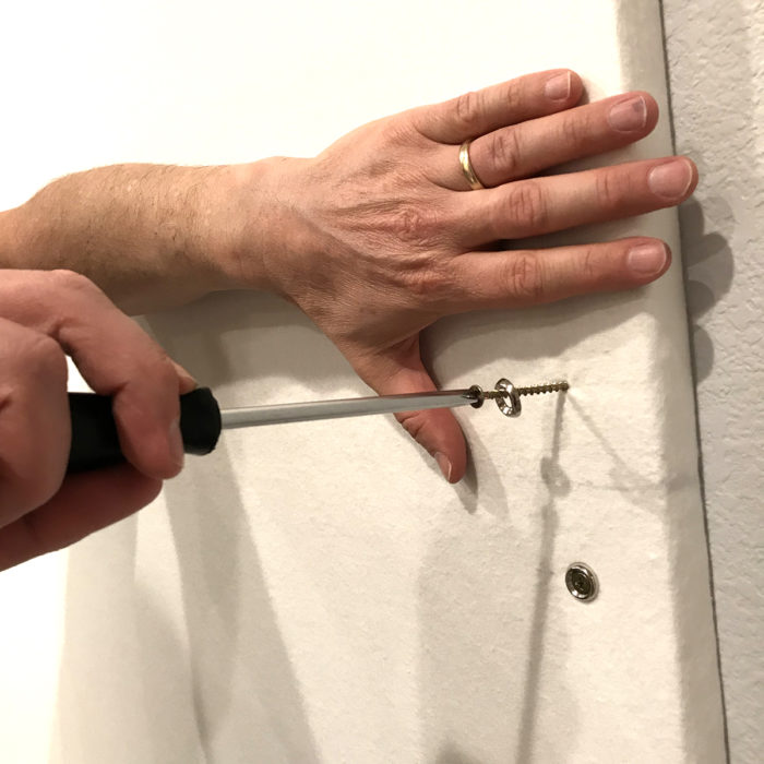 How to Build a Quilt Design Wall by Christa Watson by popular quilting blog, Diary of a Quilter: image of a man securing their quilt design board to a wall with a screw driver, screws, and washers.