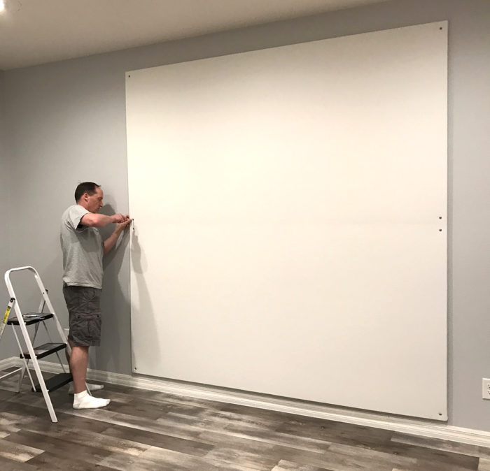 How to Build a Quilt Design Wall by Christa Watson by popular quilting blog, Diary of a Quilter: image of a man securing their quilt design board to a wall with a screw driver, screws, and washers.