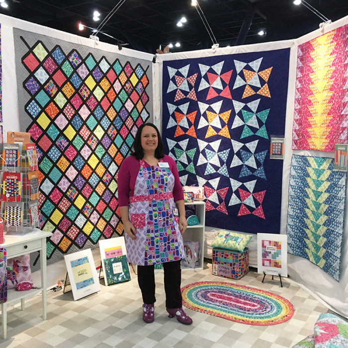 How to Build a Quilt Design Wall by Christa Watson by popular quilting blog, Diary of a Quilter: image of a woman standing in front of her quilt design walls with various quilts hanging on them.