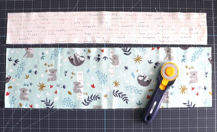 Bricks Baby Quilt Tutorial by popular quilting blog Diary of a Quilter: image of two strips of fabric on a cutting board with a rotary cutter lying on top.