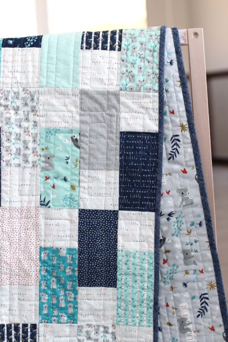 Bricks Baby Quilt Tutorial by popular quilting blog Diary of a Quilter: image of a various shades of blue bricks baby quilt draped over a crib railing.