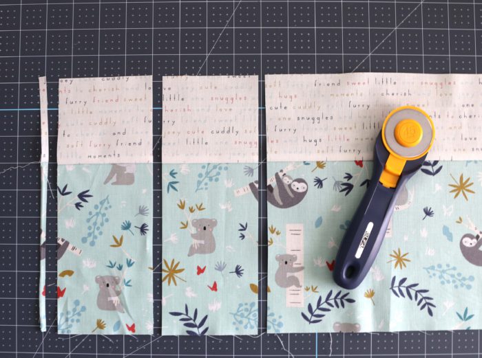 Bricks Baby Quilt Tutorial by popular quilting blog Diary of a Quilter: image of two strips of cut fabric on a cutting board with a rotary cutter lying on top.