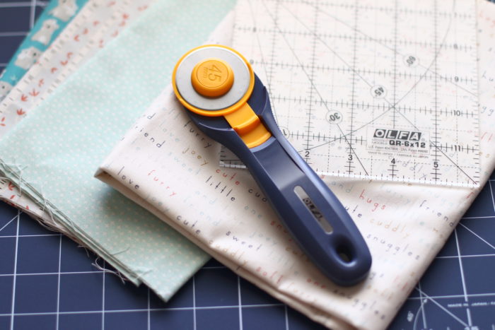 Bricks Baby Quilt Tutorial by popular quilting blog Diary of a Quilter: image of rotary cutter on top of various fat quarters quilting fabric.