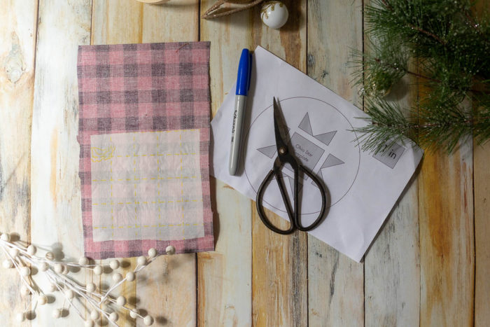 DIY Heirloom Christmas Ornament guest post by Coral + Co by popular Utah quilting blog, Diary of a Quilter: image of the backside of a piece of black and plaid fabric with Steam a Seam 2 on the bottom half of it, a blue permanent marker, sewing scissors, and circular pattern template.