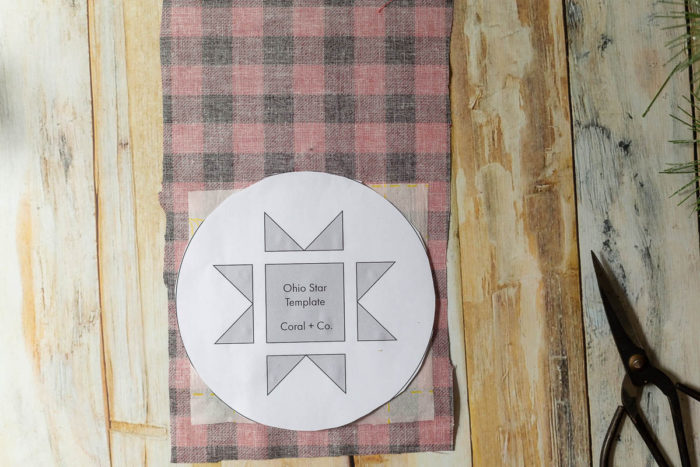 DIY Heirloom Christmas Ornament guest post by Coral + Co by popular Utah quilting blog, Diary of a Quilter: image of the backside of a piece of black and red plaid fabric with a square of Steam a Seam 2 on the bottom portion and an Ohio star template resting on top.