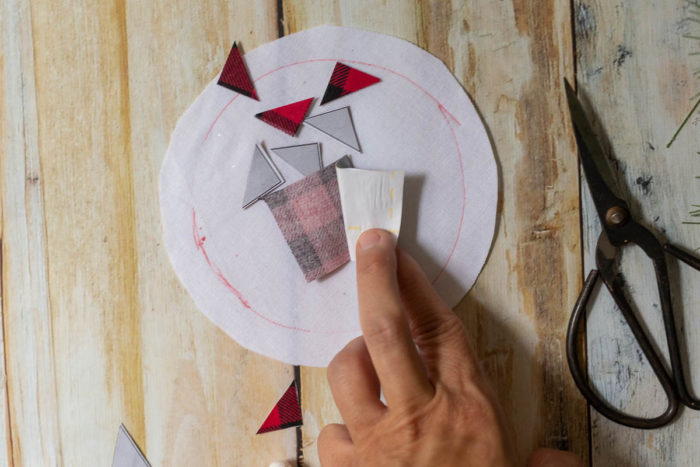 DIY Heirloom Christmas Ornament guest post by Coral + Co by popular Utah quilting blog, Diary of a Quilter: image of a woman peeling off Steam a Seam 2 paper from the back side of piece of an Ohio star pattern on black and red plaid fabric.