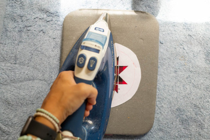 DIY Heirloom Christmas Ornament guest post by Coral + Co by popular Utah quilting blog, Diary of a Quilter: image of a woman ironing a black and red plaid Ohio star onto a piece of round white felt fabric.