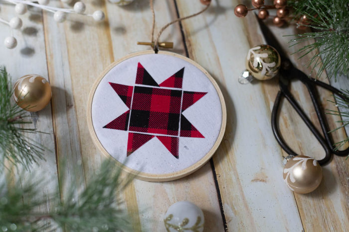 DIY Heirloom Christmas Ornament guest post by Coral + Co by popular Utah quilting blog, Diary of a Quilter: image of a finished embroidery hoop heirloom christmas ornament with a red and black plaid Ohio star, sewing scissors, white and gold ornaments, and pine tree branches.