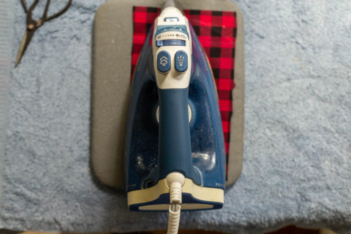 DIY Heirloom Christmas Ornament guest post by Coral + Co by popular Utah quilting blog, Diary of a Quilter: image of an iron resting on top of a piece of black and red plaid fabric.