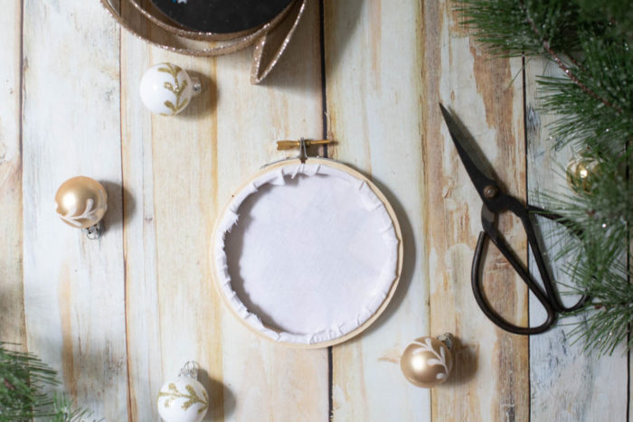 DIY Heirloom Christmas Ornament guest post by Coral + Co by popular Utah quilting blog, Diary of a Quilter: image of the backside of a finished embroidery hoop heirloom christmas ornament, sewing scissors, white and gold ornaments, and pine tree branches.