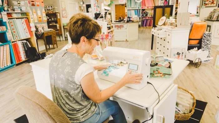 Shop Local - My Girlfriend's Quilt Shoppe + Giveaway by popular Utah quilting blog, Diary of a Quilter: image of a woman sitting at a sewing machine inside My Girlfriend's Quilt Shoppe.