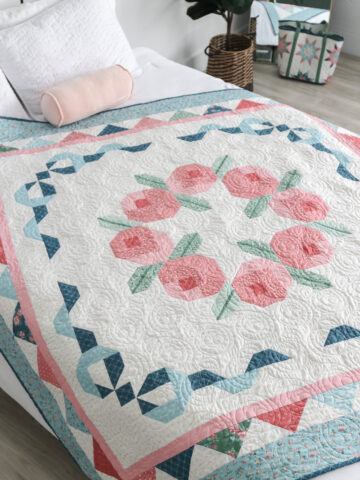 Briarcreek Blooms lap quilt with rosebud wreath center and patchwork borders in soft blue, sage, and red.