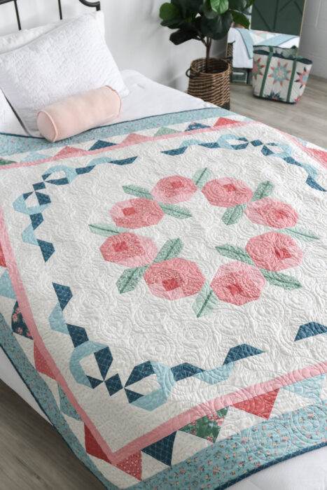 Briarcreek Blooms quilt spread on a bed; patchwork borders frame the center wreath motif.