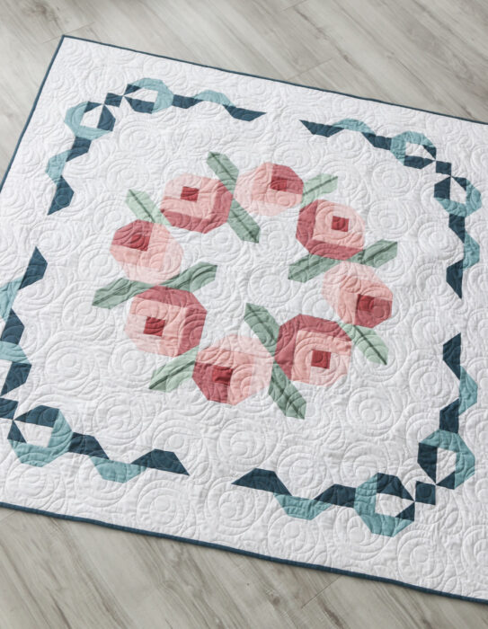 Lap-size Briarcreek Blooms laid flat; simple rosebud wreath center and pieced bow borders in Confetti Cotton solids.
