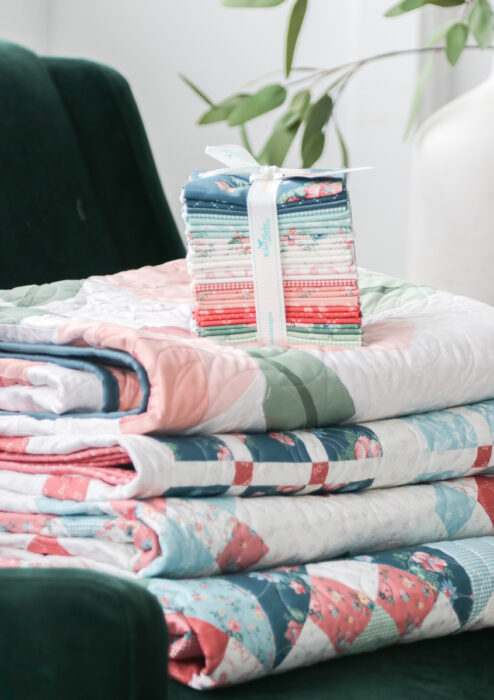 Fat Quarter bundle of Mary Catherine fabric collection by Amy Smart for Riley Blake Designs on top of a stack of coordinating quilts.