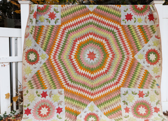 Antique Lone Star quilt in soft vintage prints draped over a wooden railing outdoors, surrounded by autumn leaves.