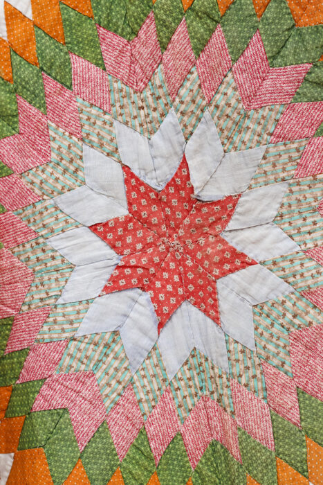 Close-up of the antique Lone Star quilt showing the tiny hand-pieced diamond patches and worn, frayed fabrics.