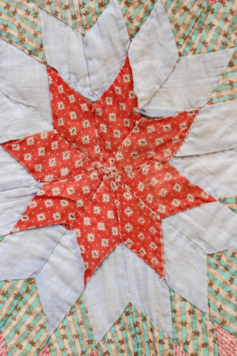 Close-up of the antique Lone Star quilt showing the tiny hand-pieced diamond patches and worn, frayed fabrics.