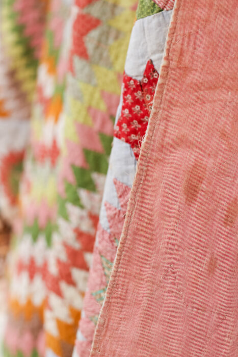 Close-up of the antique Lone Star quilt showing the tiny hand-pieced diamond patches and worn, frayed fabrics. Pink on pink backing and hand quilting