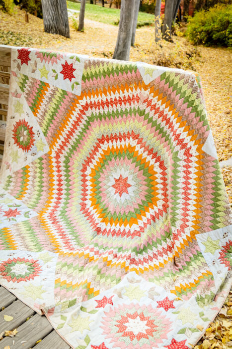 Antique Lone Star quilt in soft vintage prints draped over a wooden railing outdoors, surrounded by autumn leaves