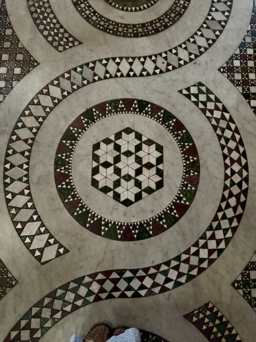 Close-up of a medieval Cosmati floor with circles, triangles, and bands of colored marble fitted into a repeating geometric pattern.