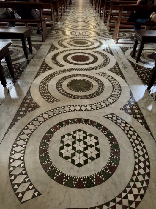 Cosmatesque marble floor in the Basilica of Santa Maria in Trastevere, featuring colorful geometric inlays arranged around large circular stone disks.