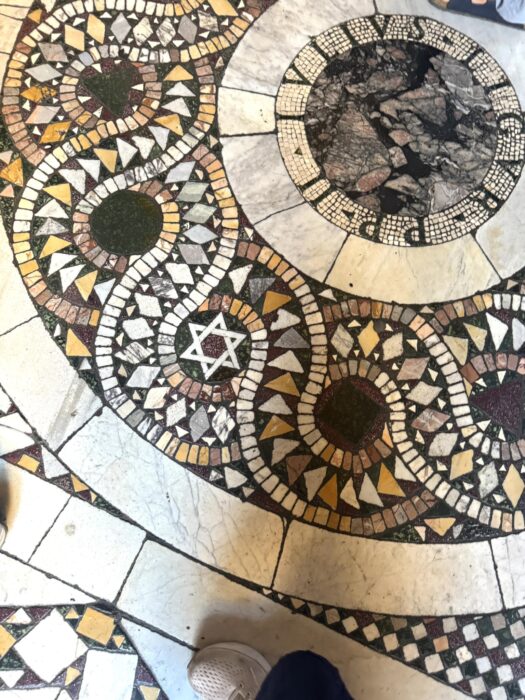 Intricate Cosmatesque church flooring in Rome, with red and green marble pieces forming interlocking shapes and decorative borders.